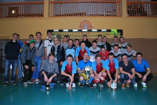 Foto: Gruppenbild mit mehreren Mannschaften vor einem Handballtor in einer Sporthalle.