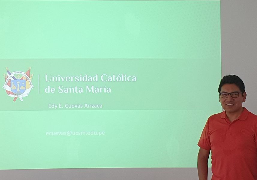 Mann im roten T-Shirt steht vor einer grünen Leinwand mit dem Logo der Santa Maria Universität aus Peru