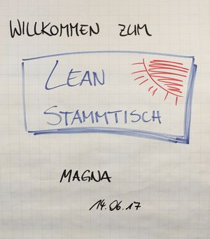 Foto: Auf einem Clipboard Papier steht. "Willkommen zum LEAN Stammtisch".