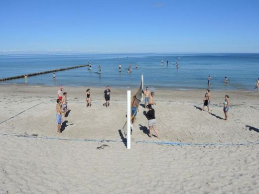 Foto: Zwei Beachvolleyball Mannschaften spielen am Strand.