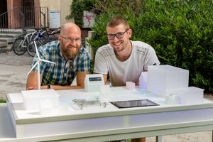 Foto: Zwei Studierende stehen draußen an einem Labortisch mit Modellen für Energie Infrastruktur.