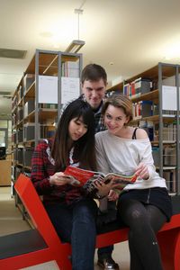 Foto: Drei Studierende sitzen zusammen in der Bibliothek und schauen gemeinsam eine Zeitschrift an.