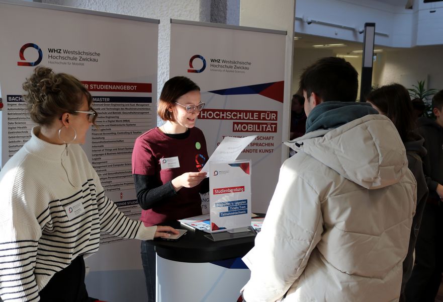 Studierende stehen vor einem Infotresen und beraten Schüler
