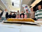 Im Vordergrund ein Kuchen mit einer 2500, im Hintergrund Schüler.