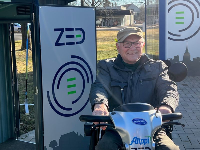 Foto: Ein Mann sitzt auf einem E-Scooter vor einer Mobilbox des Projektes ZED.