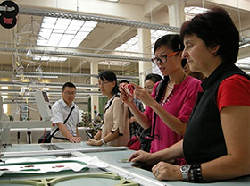 Foto: Besucher aus dem chinesischen Chengdou betrachten Stoffmuster die auf einer Maschine liegen.