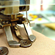Foto: Nahaufnahme. Eine Textilmaschine näht einen Knopf an.