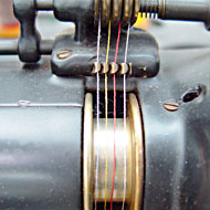 Foto: Nahaufnahme. Vier farbige Fäden gehen parallel entlang einer Rolle an einer Textilmaschine.