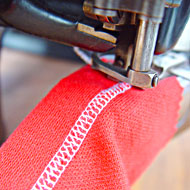 Foto: Nahaufnahme. Eine Textilmaschine stickt einen schmalen Streifen mit Muster in ein Textil.