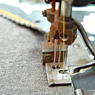 Foto: Nahaufnahme. Eine Textilmaschine vernäht den Rand eines Textil.