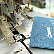 Foto: Nahaufnahme. Eine Nadel mit Faden an einer Textilmaschine. Ein Stück Textil liegt daneben.