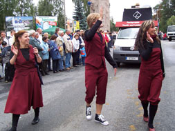 Foto: Drei nebeneinander laufende Teilnehmer des Festumzuges winken dem Publikum.