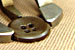 Foto: Nahaufnahme. Ein Knopf liegt auf Stoff und ist zwischen zwei Haltern einer Textilmaschine eingespannt.