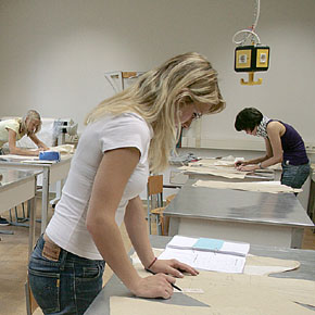 Foto: Ein Frau steht an einem Tisch und tätigt eine Schnittkonstruktion.