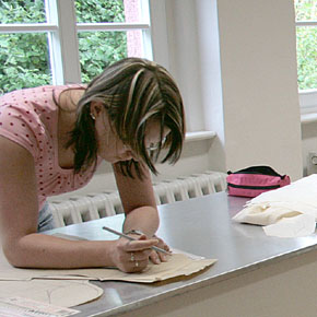 Foto: Ein Frau steht an einem Tisch und tätigt eine Schnittkonstruktion.