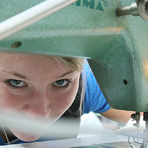 Foto: Das Gesicht einer Studierenden schaut unter einem Nähmaschinenarm hindurch.