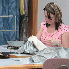 Foto: Eine Studierende sitzt an einem Tisch und betrachtet ein textiles Material.