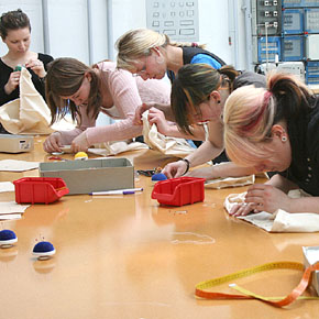 Foto: Fünf Studierende an einem großen Tisch tätigen Zuschnitte und Nahtvorbereitungen.