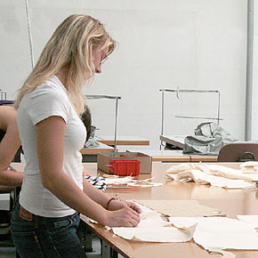 Foto: Eine Studierende tätigt an einem Tisch stehend Zuschnitte.