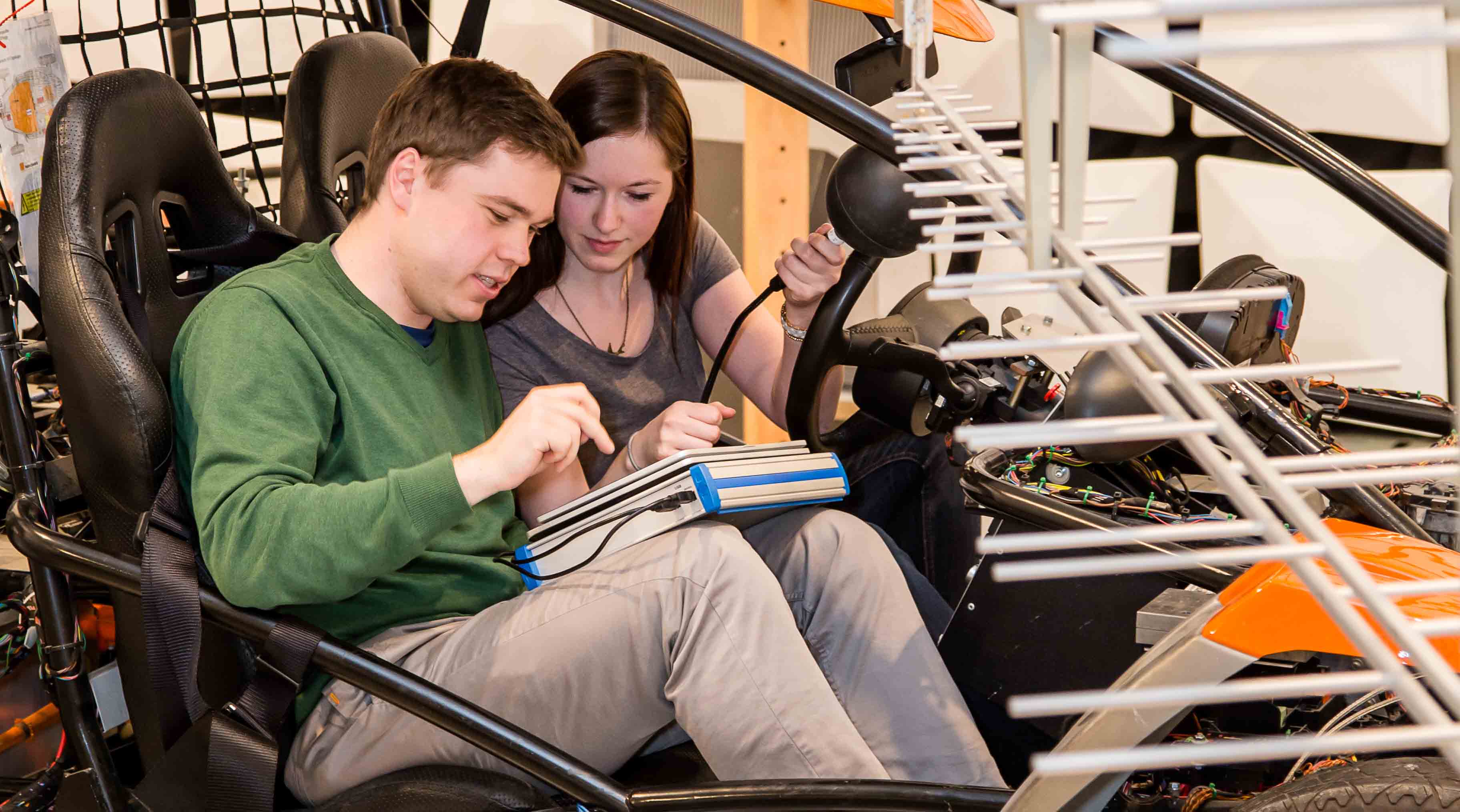 Foto: Blick ins Zentrum für Kraftfahrzeugelektronik. Zwei Studierende sitzen in einem Fahrzeug und tätigen mit einem Messgerät elektromagnetische Untersuchungen.