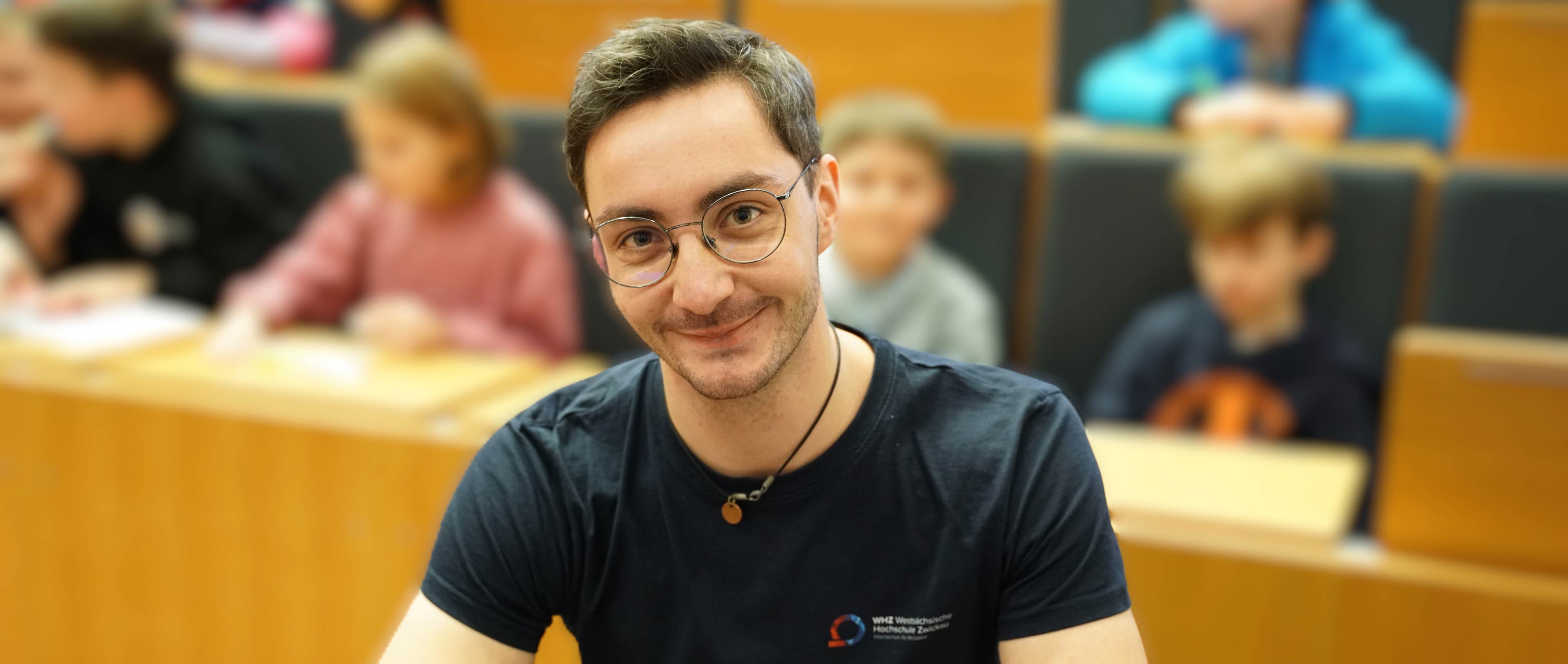 Foto: Ein Student sitzt im Höhrsaal und lächelt in die Kamera (Quelle: WHZ/Jeschke)