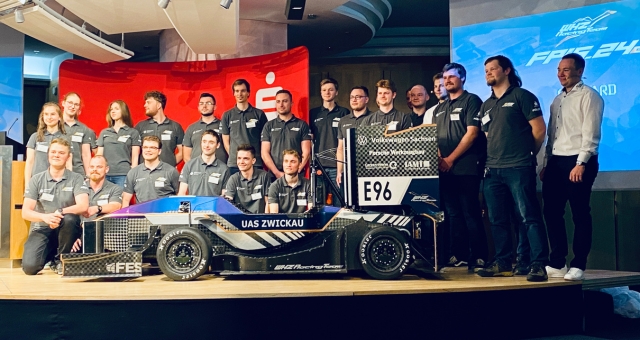 Gruppenbild des WHZ Racingteams blicken in die Kamera, im Vordergrund das. neue Rennfahrzeug