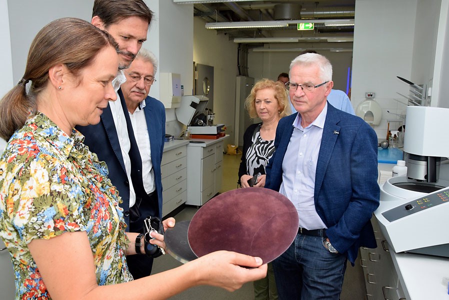 Foto: Eine Mitarbeiterin zeigt im Labor 4 weiteren Personen flache, kreisrunde Objekte zum Technologiestammtisch.