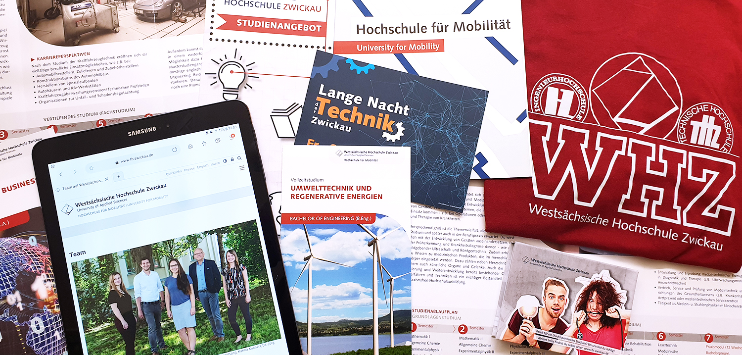 Foto: Verschiedene Flyer und ein Tablet mit offener Webseite auf einem Tisch liegend.