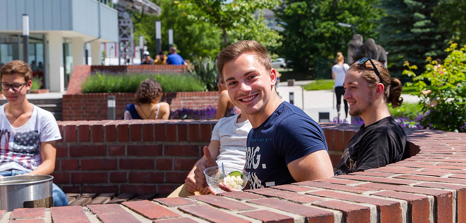 Titelbild CampusTour, Quelle: WHZ/Helge Gerischer. Vor der Mensa auf dem Campus Scheffelberg sitzen Studierende im Außenbereich.