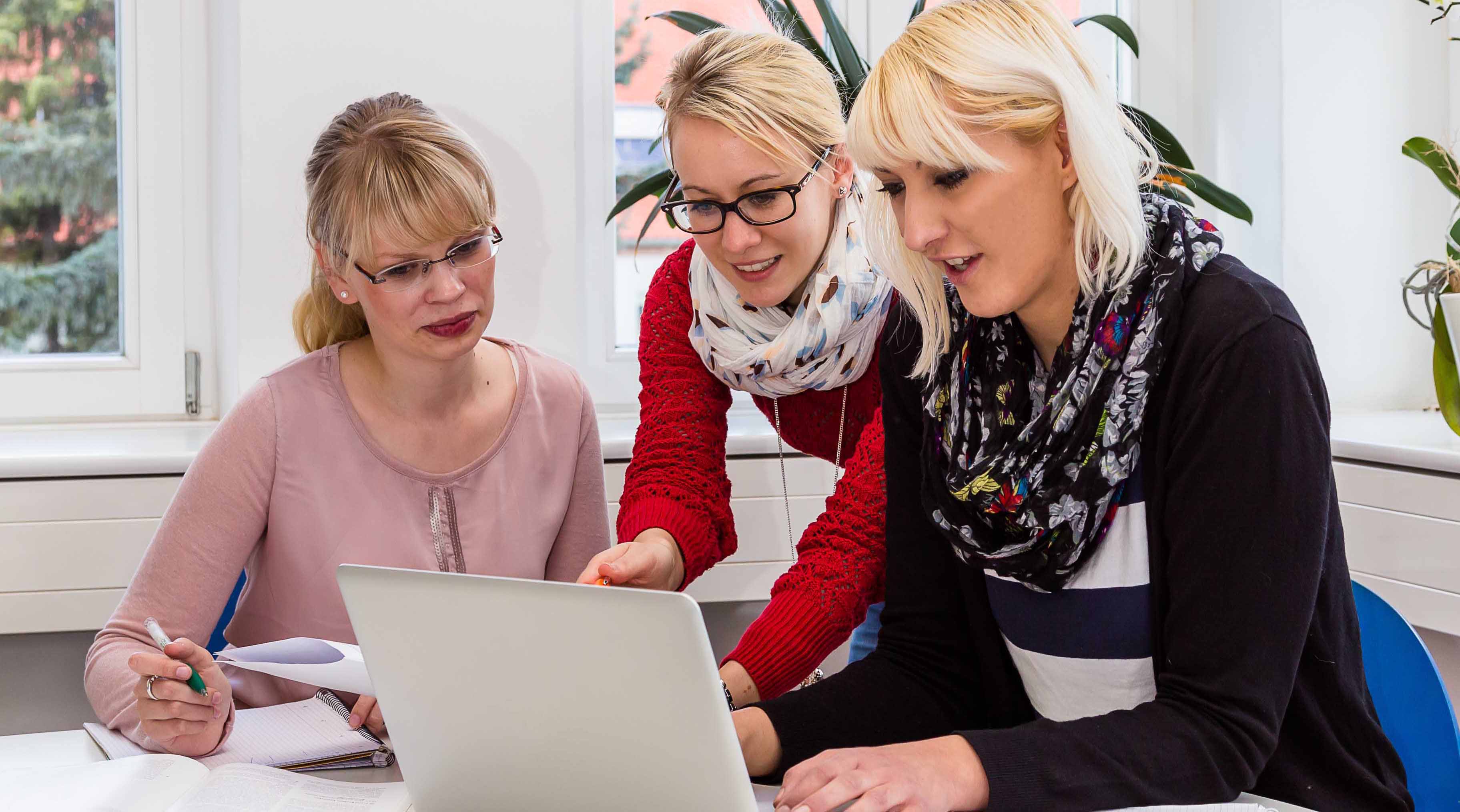 Foto: Drei Frauen sitzen zusammen in einem Büro, dabei schauen Sie auf einen Laptop Monitor und betrachten den Bildschirminhalt.