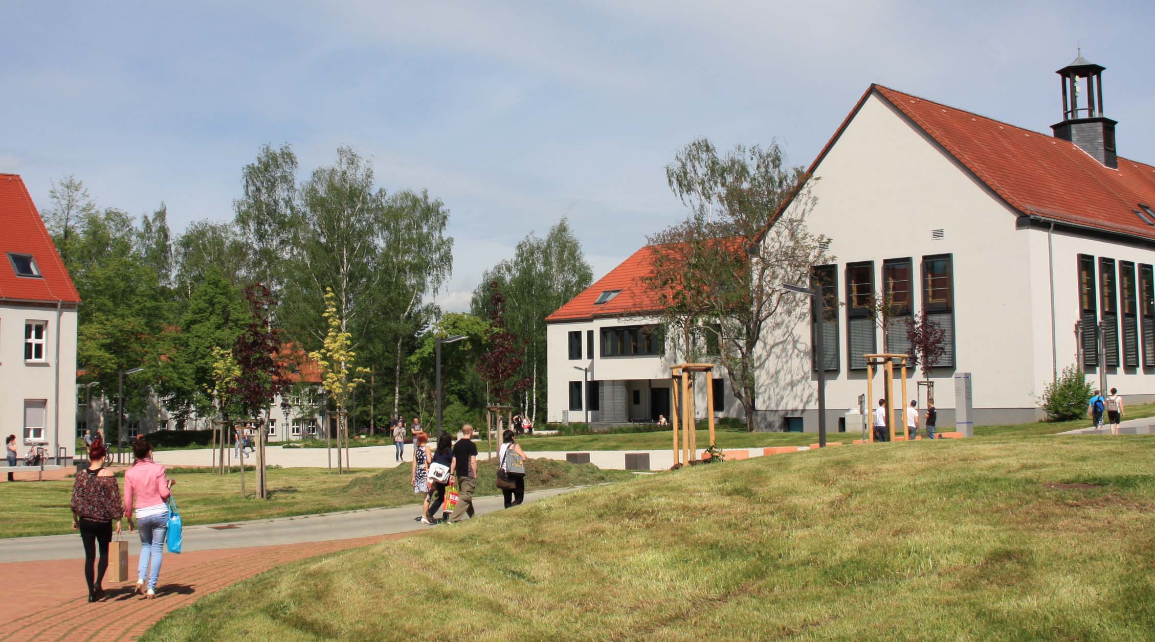 Foto: Außenbereich des Campus Scheffelberg mit umherlaufenden Studierenden. Blick auf Lehrgebäude recht´s und kleinen Ausschnitt des Haus 3 am linken Bildrand.