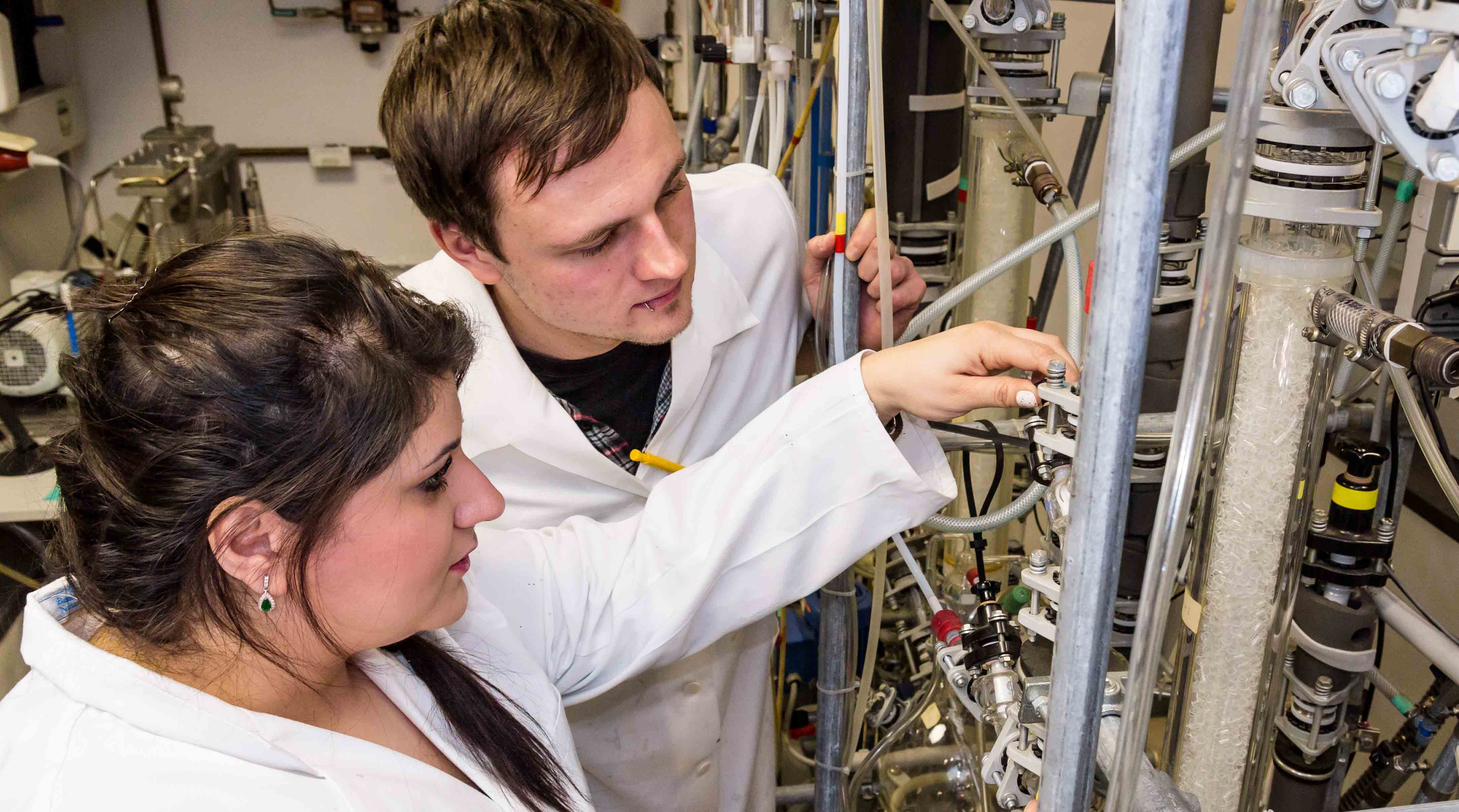 Foto: Zwei Studierende des Bereiches Umwelttechnik und Recycling stehen an einer technischen Anlage und nehmen mechanische Anpassungen vor.