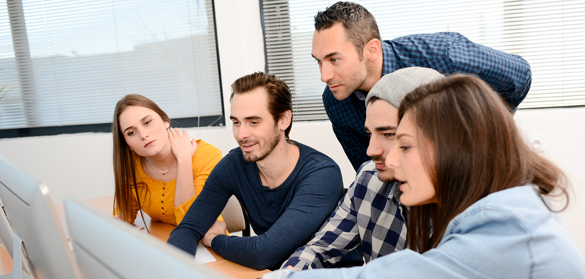 Foto: Fünf Studierende sitzend und stehend vor einem Computerbildschirm und betrachten den Bildinhalt gemeinsam.