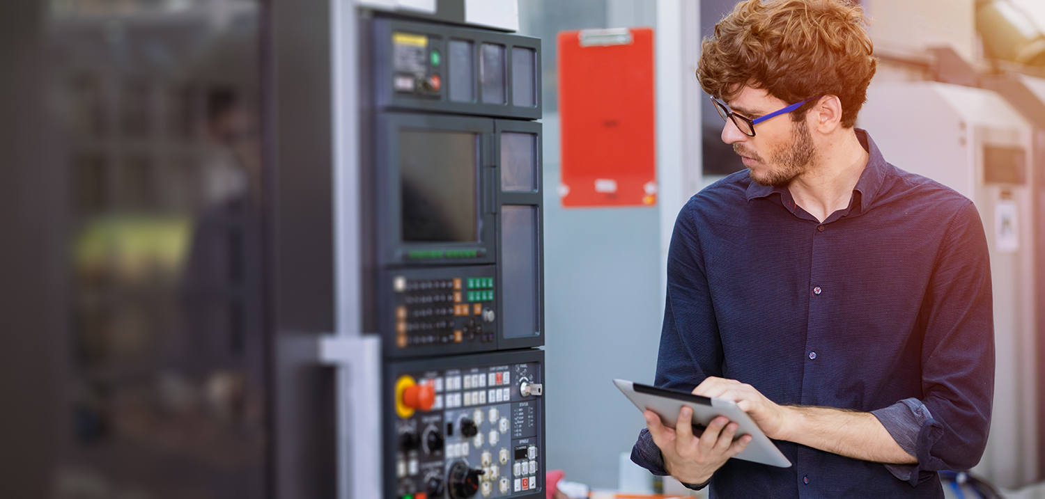 Ein junger Ingenieur mit Tablet betrachtet eine Maschine. 