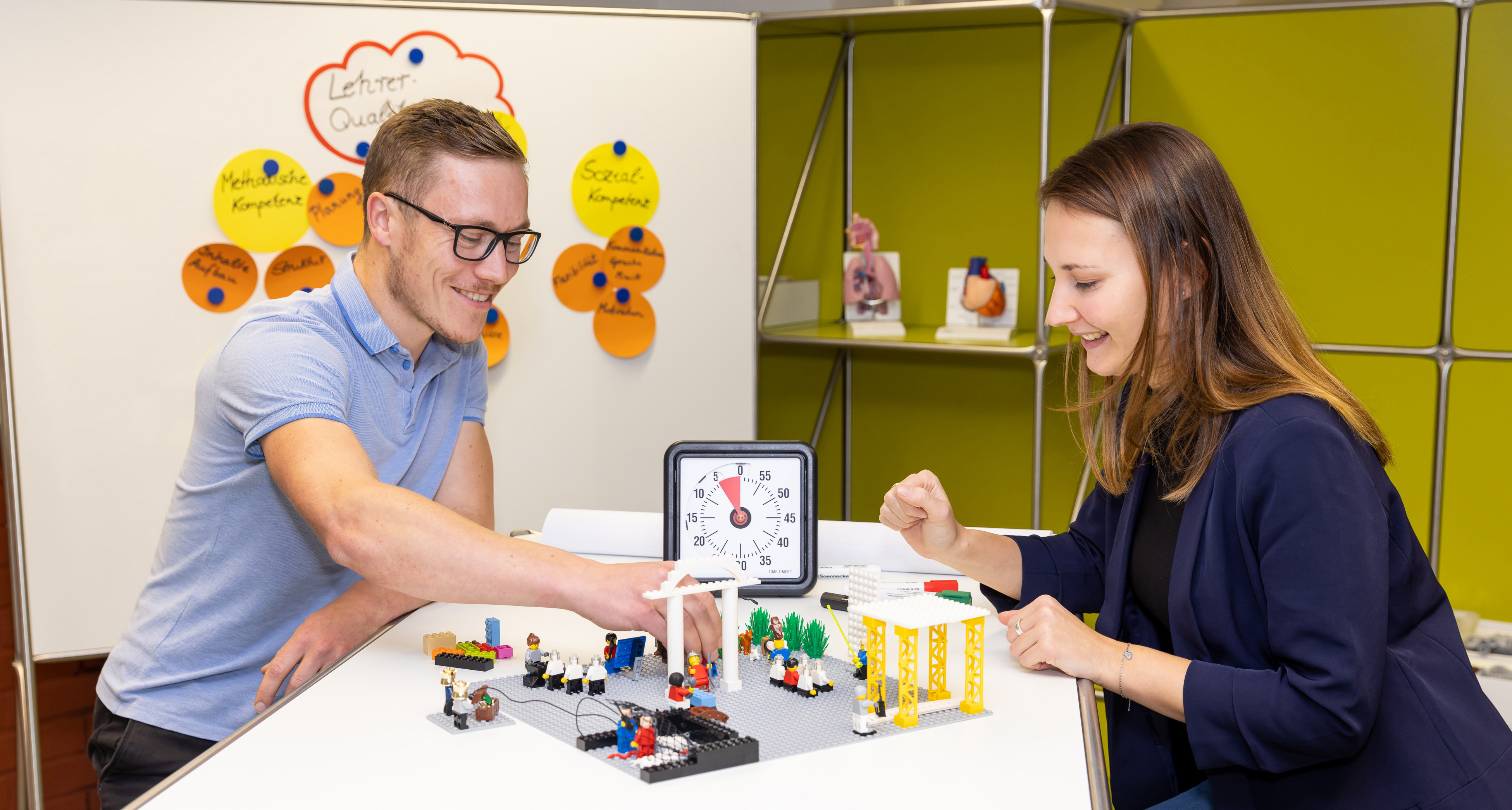 Zwei Studierende sitzen an einem Tisch und stellen Abläufe in einem Krankenhaus mit Lego-Bausteinen dar. 
