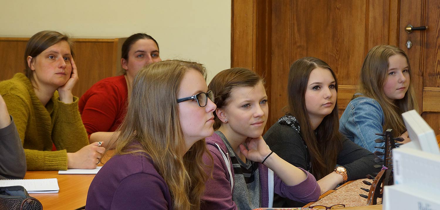 Foto: Schülerinnen sitzen in Bankreihen und hören einer Vorlesung zu. 