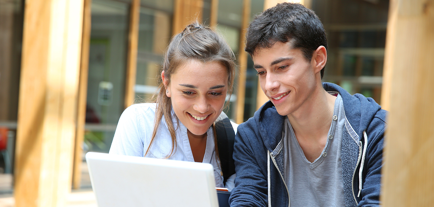 Junge und Mädchen schauen lächend auf einen Laptop