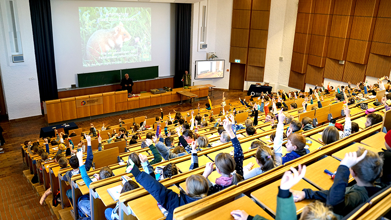 Blick in einen vollen Hörsaal, Kinder melden sich