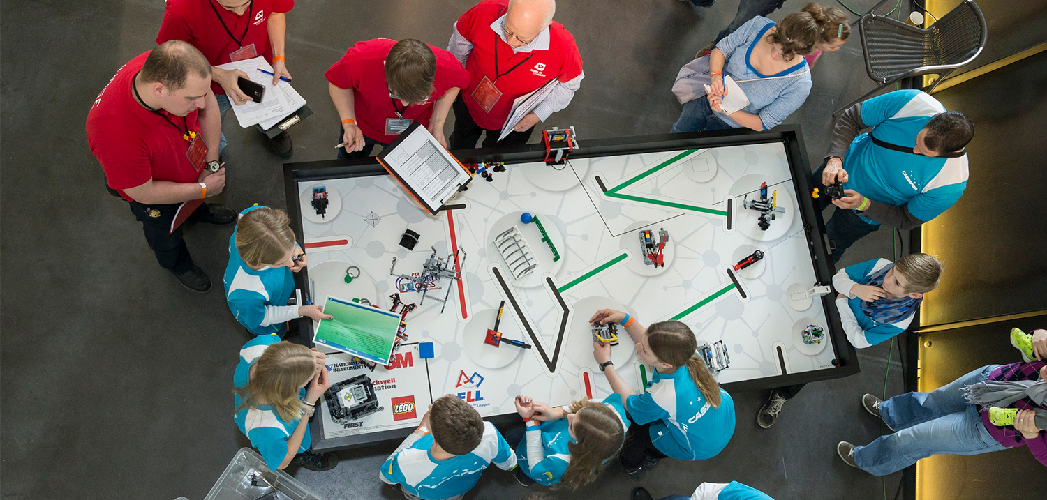 Personen stehen um einen Lego-Spieltisch im Robotern (Quelle: Hands on Technology)