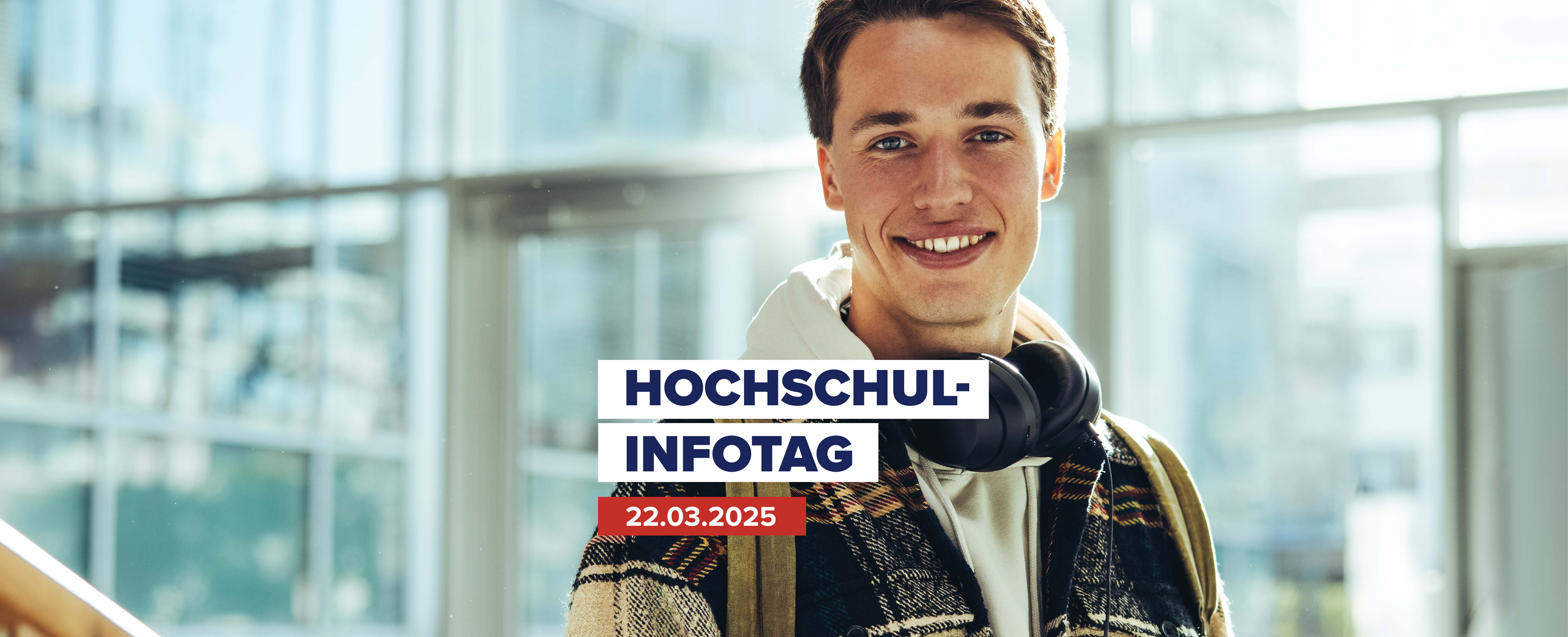 Studierender befindet sich in modernem Glasbau und schaut lächelnd in die Kamera