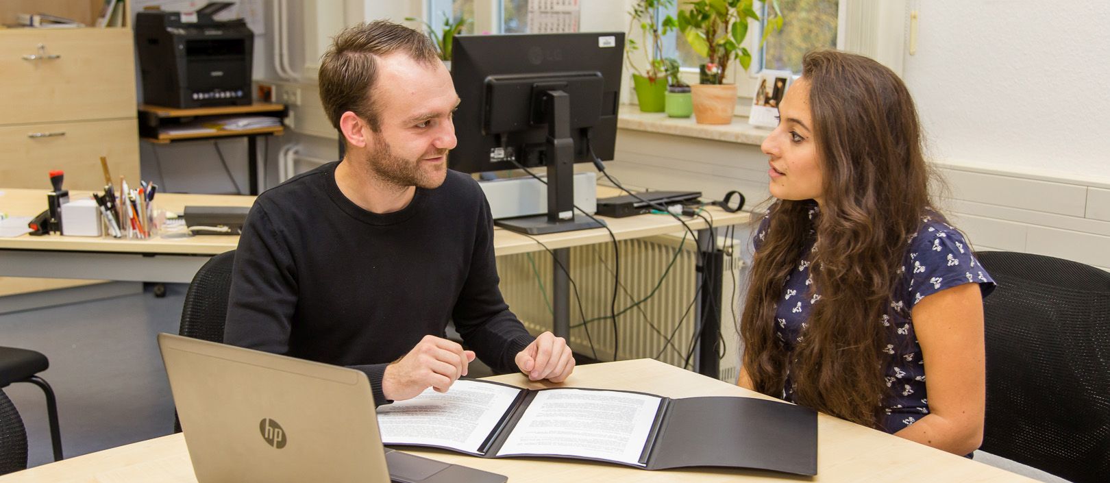 Foto: Ein Berater des Careerservice sitzt mit einer Studierenden an einem Tisch und führt eine Bewerbungsmappen-Überprüfung durch.